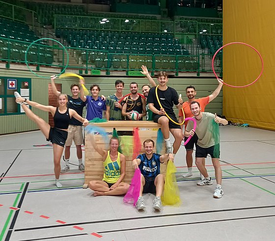 Sportstudierende posieren mit bunten Bändern und Reifen in einer Sporthalle