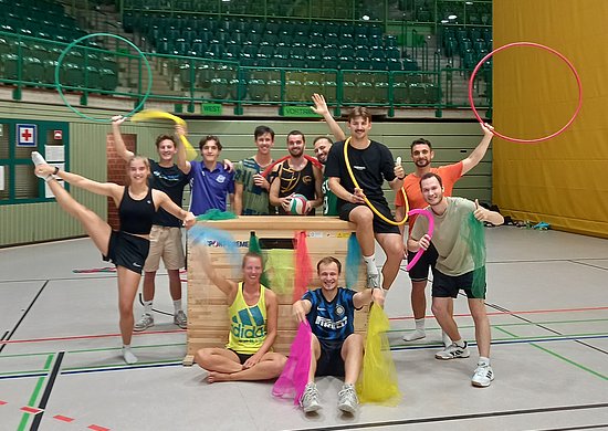 Sportstudierende posieren mit bunten Bändern und Reifen in einer Sporthalle